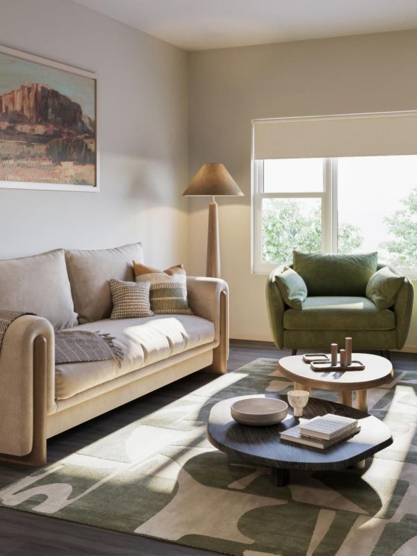 Cozy living room with beige sofa, green armchair, two round tables, and soft natural light from a window.