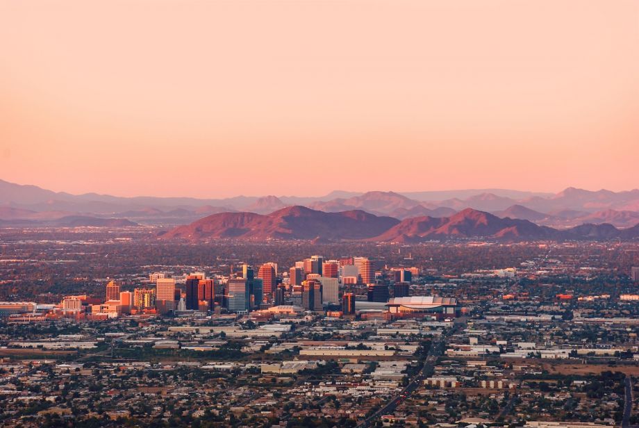 Downtown city skyline at sunset with mountains in the background and a sprawling cityscape in the foreground.