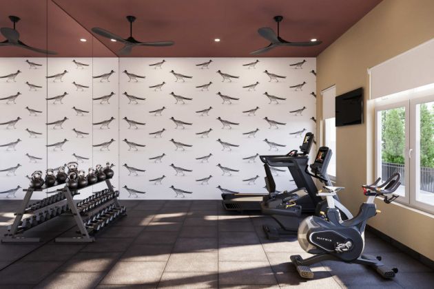 Home gym with treadmills, stationary bike, free weights, mirrored wall, and wallpaper with bird illustrations. Large window lets in light.
