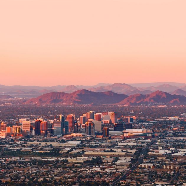 Downtown city skyline at sunset with mountains in the background and a sprawling cityscape in the foreground.