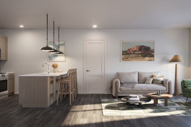 Open-plan kitchen and living room featuring light wood cabinets, a kitchen island, a neutral sofa, a green armchair, and a tall indoor plant.
